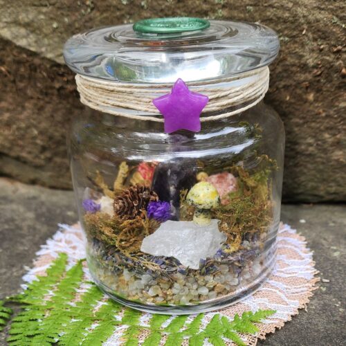 Close up of jar filled with moss, crystals, stone mushroom, pinecone and botanicals to make a magical scene