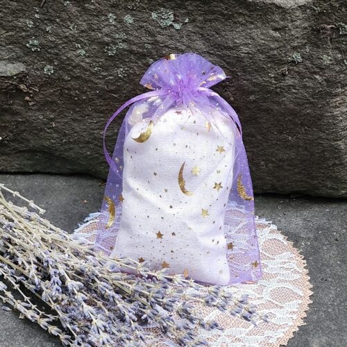 Close up of lavender sachet in purple organza bag with gold moon and stars next to dried lavender sprigs