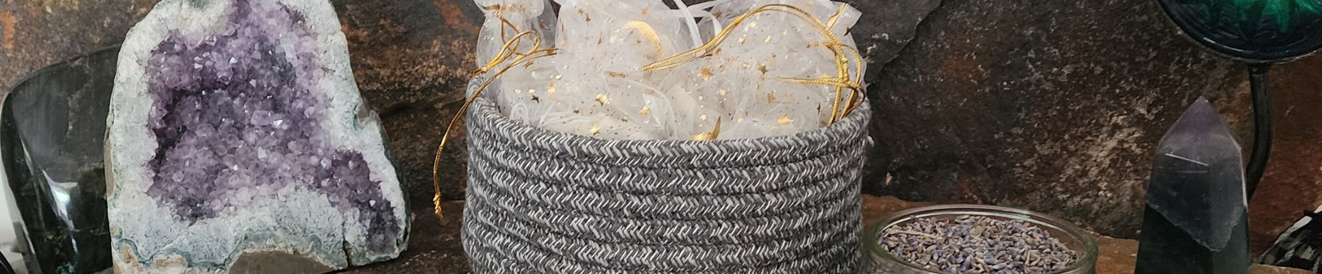 Woven basket filled with fabric beside crystals and botanicals on a natural stone background