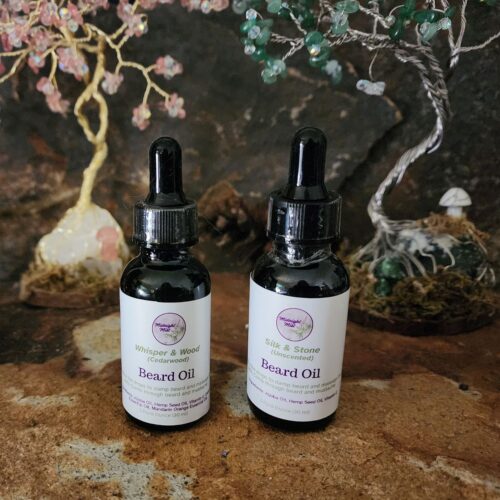 Two Midnight Mist beard oil bottles in cobalt glass dropper bottles, displayed on a rustic stone surface with handcrafted crystal Tree of Life sculptures in the background, creating a woodland-inspired setting.