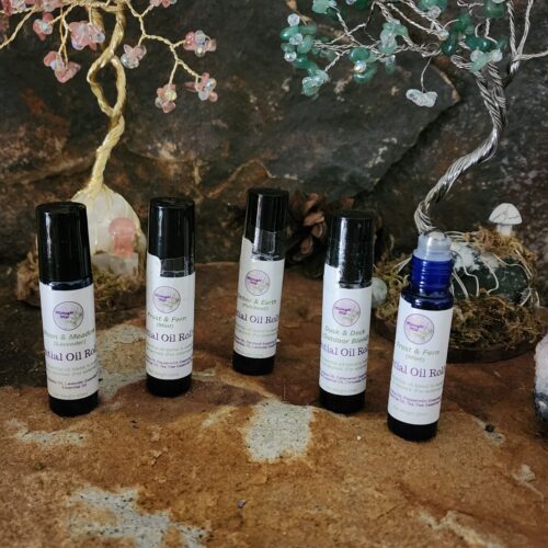 Five Midnight Mist essential oil roll-ons displayed on a natural stone surface in a woodland-inspired setting. Featured blends include Moon & Meadow, Frost & Fern, Ember & Earth, and Dusk & Deck, with handcrafted crystal Tree of Life sculptures in the background.