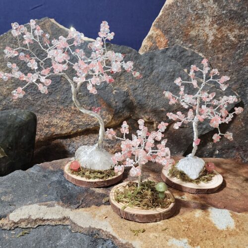 Handcrafted silver wire and cherry quartz gemstone Tree of Life in Sapling (small), Woodland (medium), and Ancient (large) sizes on natural wood bases with natural moss and stone mushrooms.