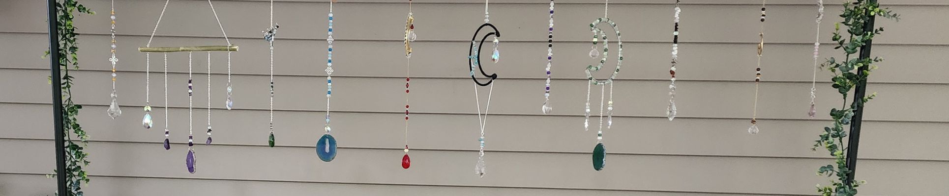 Display of eleven crystal and bead suncatchers hanging from a bar against a beige background